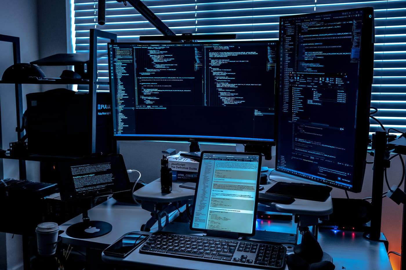 Multi-monitor engineering desk with code on screen, dark blue tones